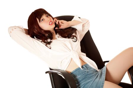 Young woman sits on armchair with mobile phone, isolatedの写真素材