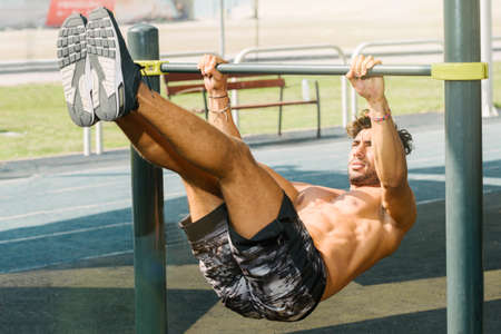 Portrait of a young arab sports doing push ups exercise on horizontal baroutdoors in Dubai during summer time.の写真素材