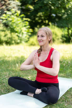 50 years old woman praying on mat outdoors in a park on a grass.の写真素材