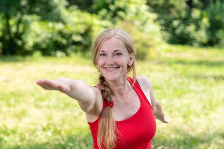 Middle aged woman in a red top practice yoga poses outdoor in a park.の写真素材
