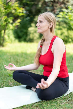 50 years old woman meditate on mat outdoors in a park on a grass.の写真素材