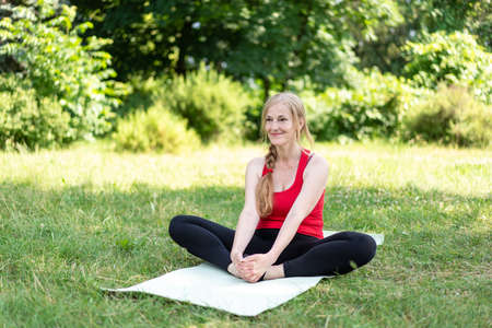 50 years old woman stretching her body on grass in a park on a yoga mat.の写真素材