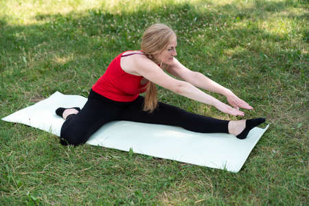50 years old woman practice yoga on mat outdoors in a park on a grass.の写真素材
