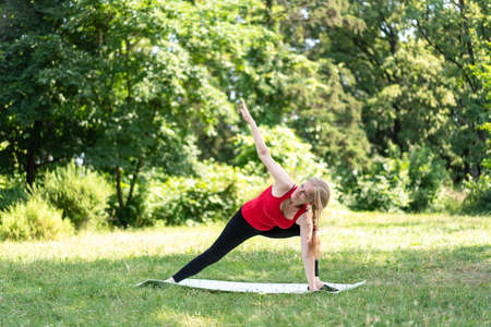 50 years old woman practice yoga on mat outdoors in a park on a grass. Archer poseの写真素材