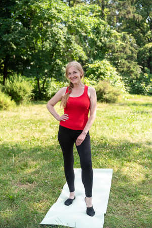 50 years old woman standing on a mat before stretching outdoors in a park on a grass.の写真素材