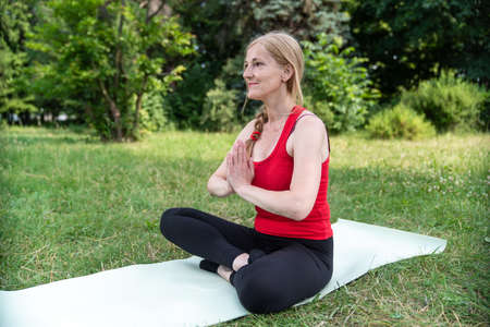 50 years old woman in red top relaxing and looking in to the camera during the meditation outdoors.の写真素材