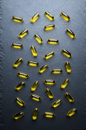 Omega 3 Gelatin Capsules Scattered On A Black Slate Table. Fish Oil, Vitamins, Pills. Medical Series. Close Up. Top View.の写真素材
