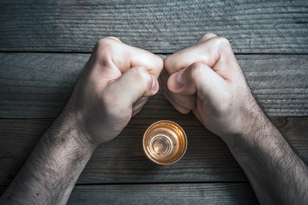 A Quit Alcohol Drinking Concept With A Booze Glass Surrounded By 2 Stressed Looking Clenched Fistsの写真素材