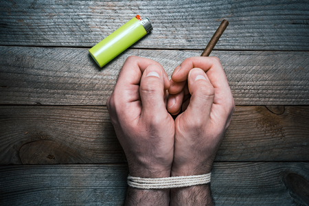 A Quit Smoking Concept With 2 Tied Hands On A Wooden Table Next To A Lighter. The Right Hand Is Holding A Cigaretteの写真素材