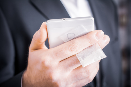 A Businessman In Suit Hiding A Little Bag Of Drugs With White Powder Behind His Mobile Phoneの写真素材