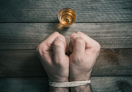 A Quit Drinking Alcohol Concept With A Booze Glass In Front Of 2 Tied Stressed Looking Clenched Fistsの写真素材