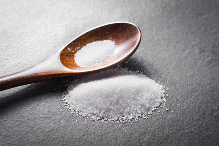 Macro Of A Wooden Spoon And A Pile of White Spilled Sugar On Slate Stone, Side Viewの写真素材