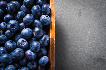 Top Down View Of A Bunch Of Blueberries In A Wooden Bowl, Standing On Slate Stoneの写真素材
