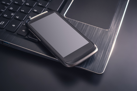 Black Smartphone With Reflection Lying On The Edge Of The Keyboard Of A Black Laptop, Top Viewの写真素材