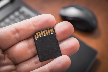Male Hand Holding An SD Card With Laptop Computer And Mouse In Background, Extent Disk Space Conceptの写真素材