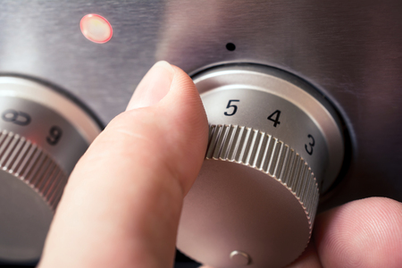 Male Hand Using Stove Controls To Set The Heat Level For A Hotplate, Set To 5 With Turned On Lightの写真素材