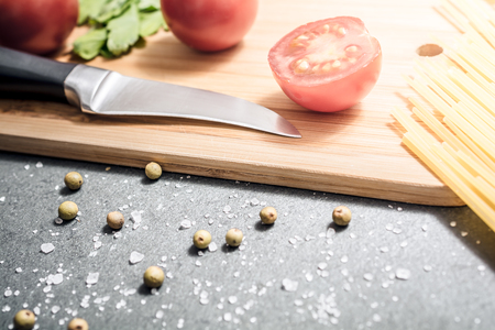 Knife On A Carving Board With Kitchen Ingredients Like Tomatoes, Pepper And Salt - Preparing Dinner Conceptの写真素材