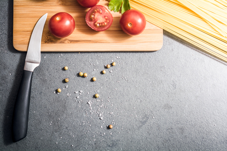 Top Down View On A Knife On A Carving Board With Kitchen Ingredients Like Tomatoes Or Noodles - Preparing Dinner Conceptの写真素材