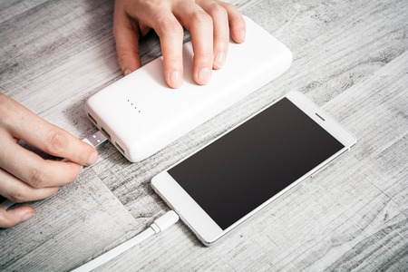 Female Hand Connecting Smartphone With Low Batteries With Powerbank To Recharge Energy, High Angle...