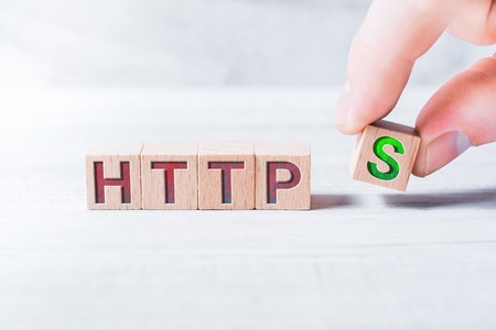 The Word HTTPS Formed By Wooden Blocks And Arranged By Male Fingers On A White Table