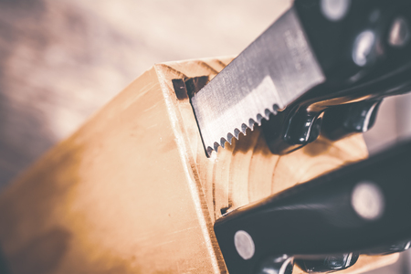 Macro Of A Jagged Steak Knife Half Pulled Out Of A Kitchen Knive Block On A Tableの写真素材