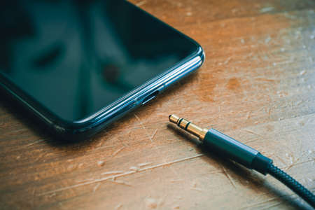 Headphone Cable Lying In Front Of A Smartphone Without Headphone Jack On Wooden Tableの写真素材