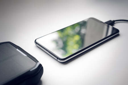 Solar Powerbank Charging Smartphone Next To A Window