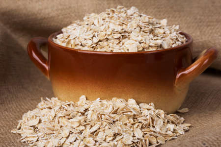a handful of oatmeal in pot on the background of sackclothの写真素材