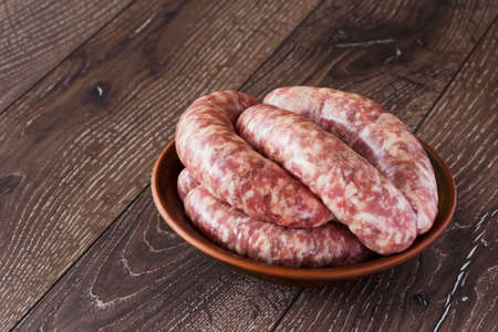 uncooked sausages in a clay plate on the wooden tableの写真素材
