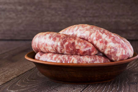 uncooked sausages in a clay plate on the wooden tableの写真素材