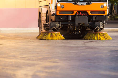 Yellow urban sweeper cleans road from dirt with a round brushの写真素材