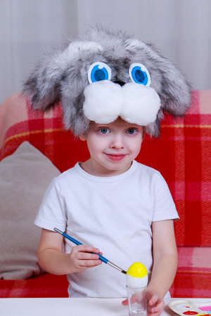 Little boy paints eggs with colored paints in a bunny cap