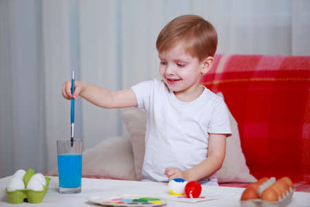 Little boy paints eggs with colored paints
