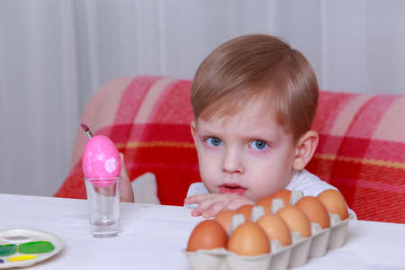Little boy paints eggs with colored paints