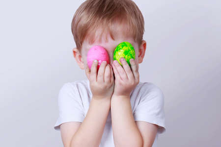 Little boy smiles and holds in his hands a two painted eggs