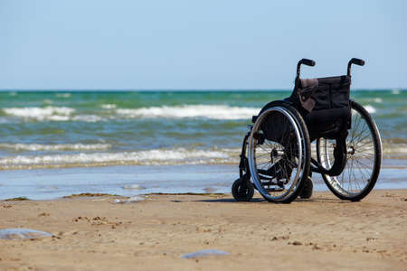 Empty black wheelchair stands on the seashoreの写真素材