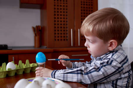 Little boy paints eggs with colored paints
