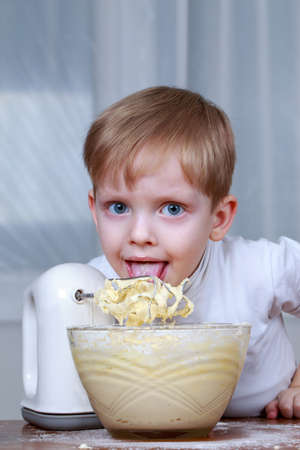Little boy licks a cream from the mixer