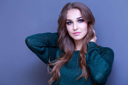 Beautiful girl with make-up in a green sweater on gray background