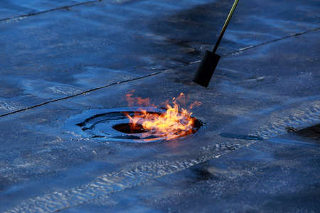 Gas burner with fire on the background of roofing material