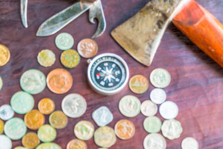 Many silver and golden coins and travel accessories on red wooden board.の写真素材