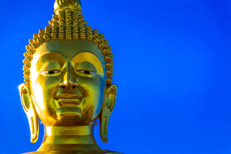 Golden large Buddha statue on temple for building, with clear blue sky.の写真素材