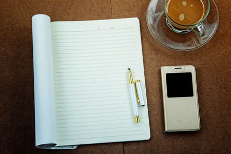 blank paper with smart phone pen and coffee cup on wooden table, business conceptの写真素材