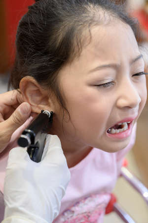 Adorable little Asian girl having ear piercing process.の写真素材