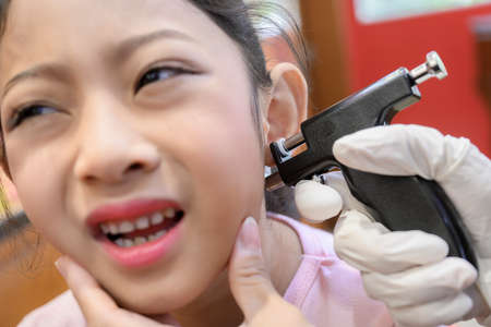 Adorable little Asian girl having ear piercing process.の写真素材