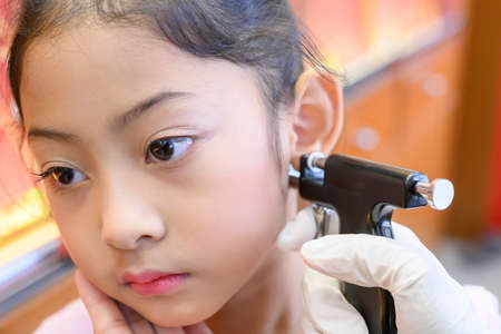 Adorable little Asian girl having ear piercing process.の写真素材