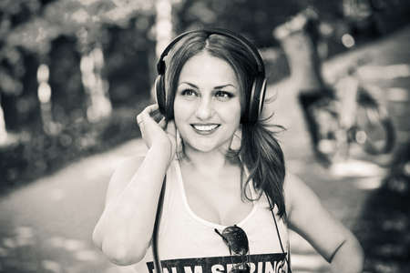 Portrait of a beautiful young smiling girl outdoors in a T-shirt, listening to music on headphonesの写真素材