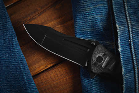 Black folding knife in his pocket on a wooden backgroundの写真素材