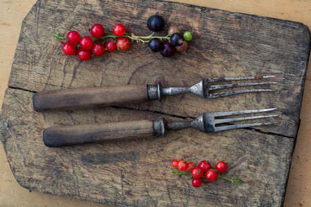 Retro forks with wooden handles and a currant berry on an old cutting board. Top view, minimalism. Vintage still lifeの写真素材