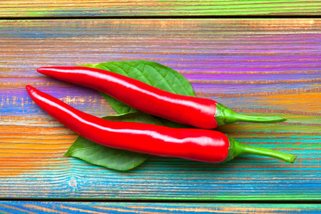 Ripe red chili peppers on a bright colorful wooden backgroundの写真素材